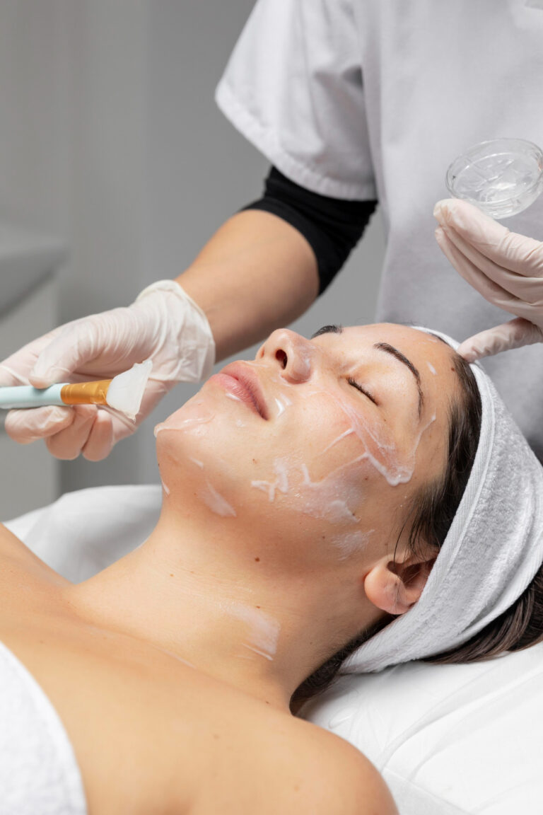 Peelingi chemiczne wykonywane w gabinecie kosmetycznym Holistic Beauty. Twarz z nałożonym peelingiem oraz kosmetyczka nakładająca go.